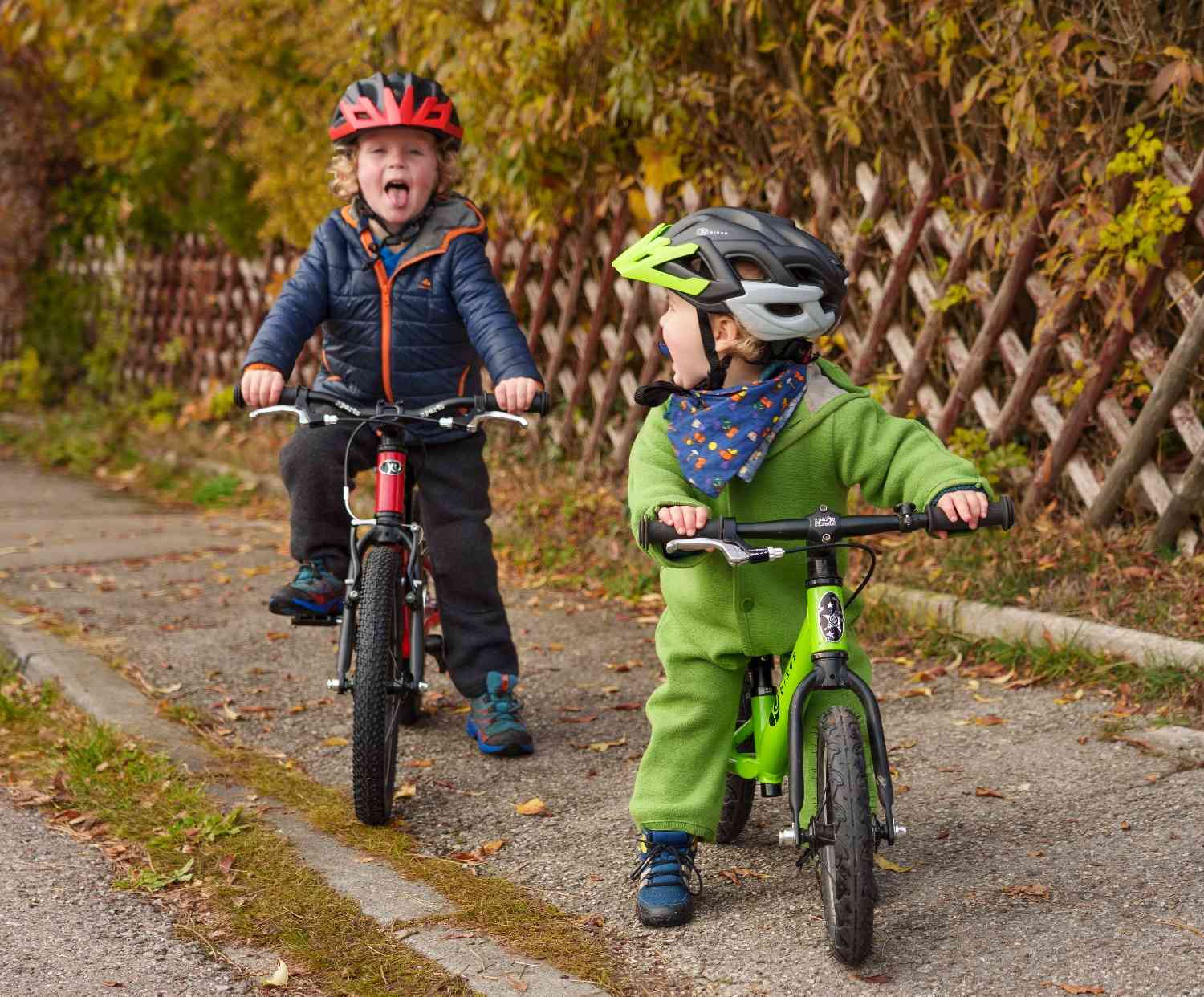Dwoje dzieci w kaskach jadących na rowerach KUbikes jesienną ścieżką — rowerek biegowy i rower dziecięcy