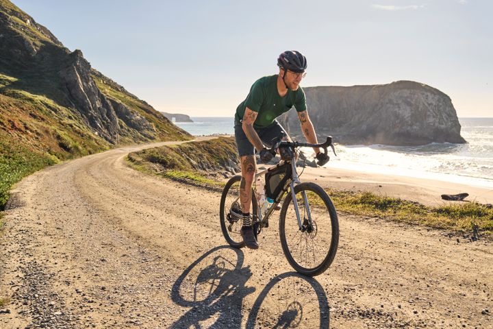 Rowerzysta na rowerze gravelowym Marin podczas jazdy po szutrowej trasie nad oceanem 4 – logo Marin Bikes – logo marki Logo Marin Bikes – amerykańskiego producenta rowerów